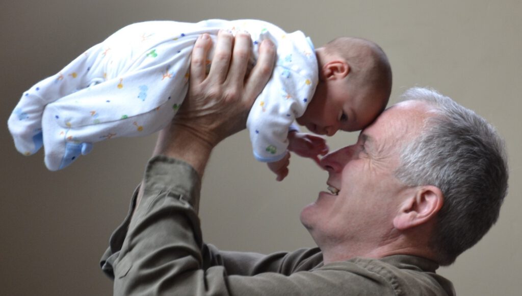 Glücklicher Großvater hebt sein Enkelkind hoch und strahtl Freude aus